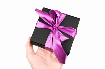 Gift black packaging with a purple bow in hand. On white background. A gift to your beloved.