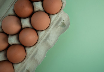 Overhead view of brown chicken eggs in an open egg carton isolated on green. Fresh chicken eggs background. Top view with copy space. Natural healthy food and organic farming concept.