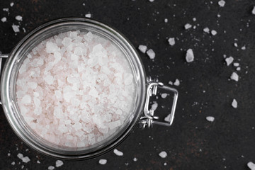 Coarse sea salt in a glass jar on a dark background. View from above.