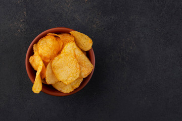 Potato chips in a clay bowl on a dark background. Free space for an inscription.