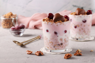 Chocolate granola with yogurt, cherries and nuts, decorated with chocolate hearts in glasses on a gray background