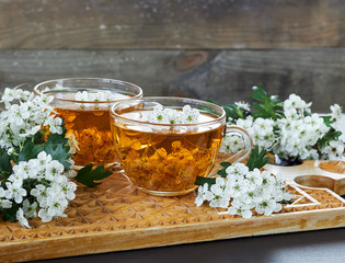 Herbal haw thorn tea from flower buds around blooming branches on wooden cutting board on rustic...