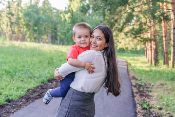 A happy young mother plays and has fun with her young son in nature, in the Park. The mother is talking to the baby. The concept of a happy family, motherhood. A mother's walk with a small child. Moth