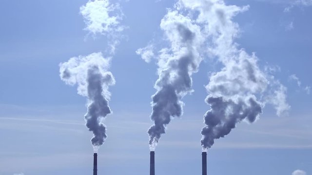 Three industrial smoke stacks of big old factory produce terrible smoke. Blue sky background and concept of environmental pollution