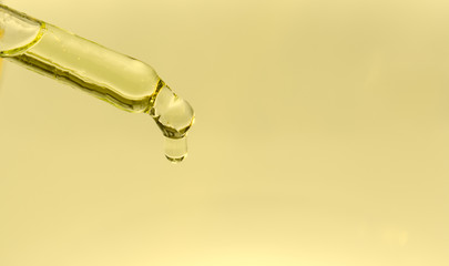 On a yellow background a glass pipette with cannabis oil. A drop drops from the end of the pipette. Concept - illicit drug use