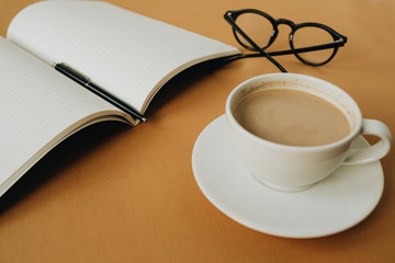 Notebook, cup of coffee, glasses on ginger background. Work, business concept.