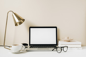 Blank screen laptop. Home office desk table workspace with coffee, lamp, glasses, notebook on beige...