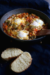 Shakshuka in a pan, with seasonal vegetables and eggs, and two slices of bread. Selective focus.