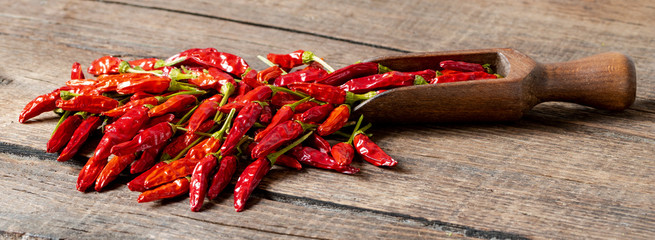 Close-up of dried red cayenne chillies and a wooden spoon on an old wooden table.