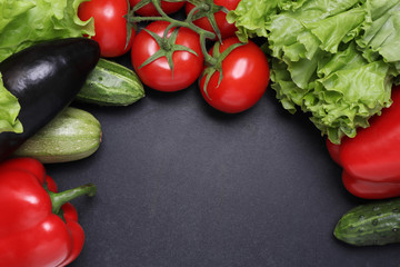 Green lettuce, red ripe tomatoes on a branch, fresh cucumbers and red bell peppers paprika. Vegetables on a black textured background.