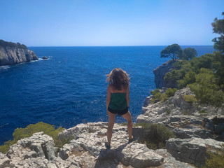 Fototapeta premium A young woman looking to a panoramic view of a beach in the middle of a mountain landscape