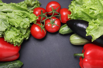 Green lettuce, red ripe tomatoes on a branch, fresh cucumbers and red bell peppers paprika. Vegetables on a black textured background.