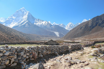 Footpath to Everest base camp near abandoned stone house. Ama Dablam mountain peak rises above mountain valley in the background. Himalayas in the morning. Theme of beautiful mountain landscapes.