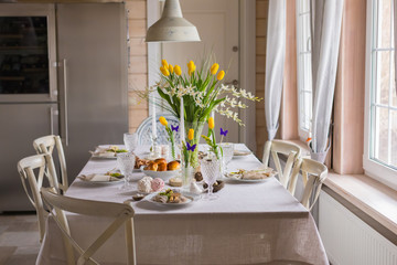 Easter festive spring table setting decoration, eggs in nest, fresh yellow tulips, marshmallows, selective focus