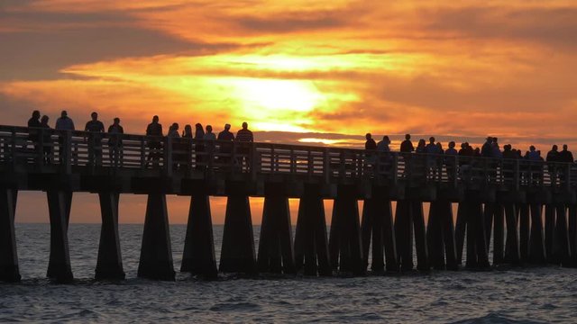 Ocean sunset. People went to the pier to watch a beautiful golden sunset in the ocean. Dark silhouettes of people walking along the pier. Beautiful sea sunset with dramatic clouds in the sky. Close up