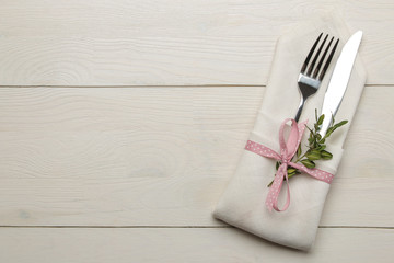 Table setting. Cutlery in a white napkin with a pink ribbon, fork and knife on a white wooden table. top view