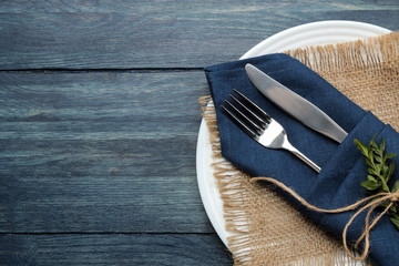 Table setting. plate and cutlery in a blue napkin, fork and knife on a blue wooden table. top view