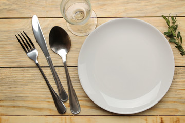 Table setting. Plate, glass and cutlery fork, spoon and knife on a natural wooden table. top view