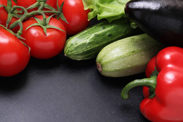 Green lettuce, red ripe tomatoes on a branch, fresh cucumbers and red bell peppers paprika. Vegetables on a black textured background.