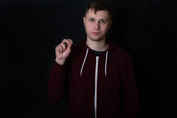 Studio portrait of a young man in a red sweatshirt against black background. Deaf and dumb guy shows 