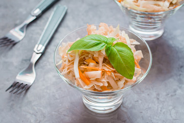 American ready-to-eat cole slaw salad of cabbage, celery, carrots and apples with basil leaves in glass bowls on the table. The concept of healthy and proper nutrition. Close-up