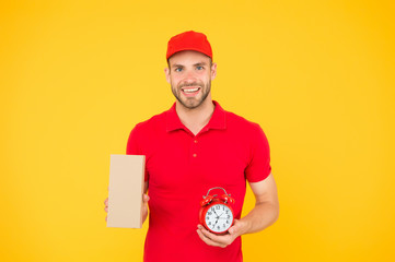 get a delivery with us. on-time delivery. man in uniform hold post box and alarm clock. delivery for In Time customers. Courier and box with time clock. Delivery man yellow background