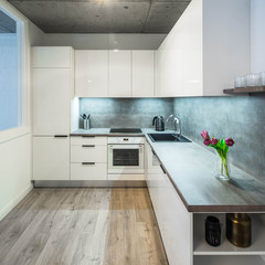 Modern interior of kitchen in private house. Clean white kitchen set. Flowers.