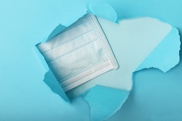 Blue medical mask peep into the slit of colored paper. Protecting health from various viruses and...