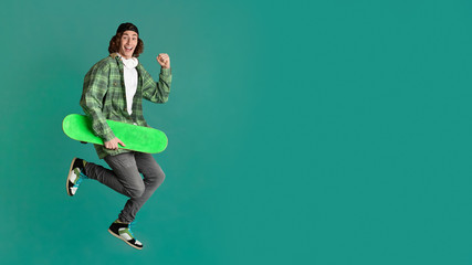 Funky smiling guy with skateboard jumping on color background, space for your design. Panorama