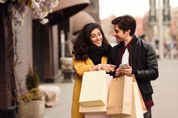 Lovely couple using smartphone and walking down the streets