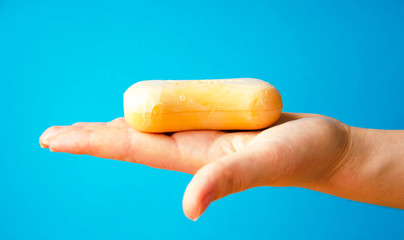Women's hands are holding soap. Soap foam on the hands. Yellow soap in the hands. Woman washes soap with hands side view on a blue background. Virus protection.  COVID-19
