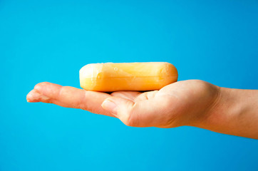 Women's hands are holding soap. Soap foam on the hands. Yellow soap in the hands. Woman washes soap with hands side view on a blue background. Virus protection.  COVID-19