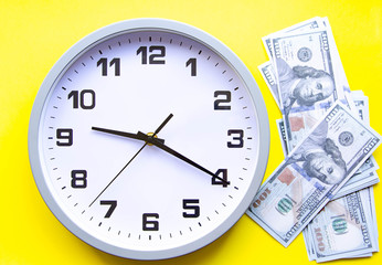Analog white clock and dollars on a gray, yellow, blue background. Banknotes next to the clock, on top. Place for text.  Business, are you ready? Copy Space