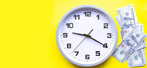 Analog white clock and dollars on a gray, yellow, blue background. Banknotes next to the clock, on top. Place for text.  Business, are you ready? Copy Space