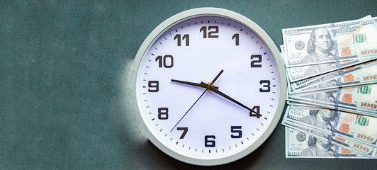 Analog white clock and dollars on a gray, yellow, blue background. Banknotes next to the clock, on top. Place for text.  Business, are you ready? Copy Space