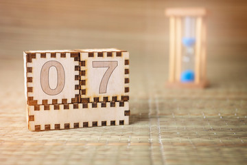 Calendar, wooden cube with date 7 and an empty space for the month, on an abstract woven hourglass background.