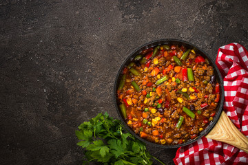 Chili con carne in skillet on dark stone table.