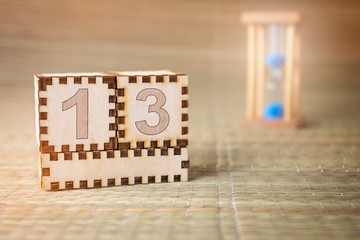 Calendar, wooden cube with date 13 and an empty space for the month, on an abstract woven hourglass background.