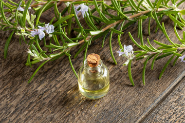 A bottle of essential oil with blooming rosemary twigs