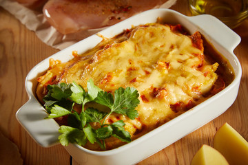 Close up of vegetable casserole with cheese salmo, chicken on kitchen table. Flatlay of salmo pudding (pie) on wooden background. Rustic homemade casserole. Healthy vegetarian cuisine.