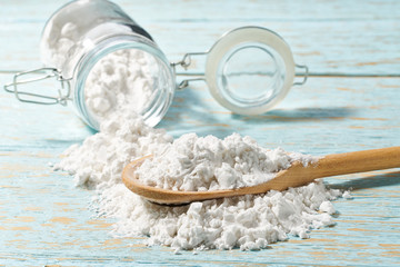 Pour  cornstarch from a glass jar into a wooden spoon, close-up.