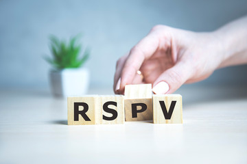 rsvp acronym request for a response from the invited person on wooden cubes with female hand.