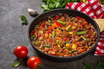 Chili con carne in skillet on dark stone table.