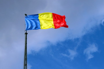 Flag of Romania on mast, in front of the blue sky. Blue background with clouds