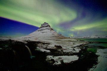 Strong Northern light pass over a beautiful mountain covered with snow with clear sky 