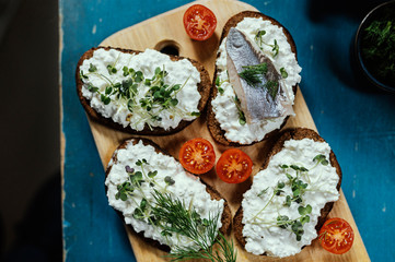 Brown bread with cottage cheese and herring on a wooden plate.