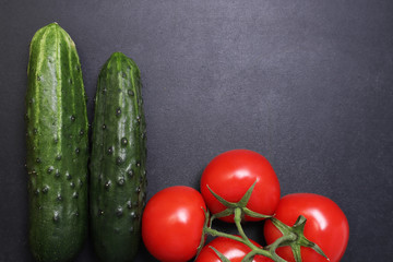 Fresh green cucumbers and red ripe tomatoes. Vegetables on a black textured background.