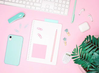 Flat layout of notepad with sticker, keyboard and palm on pink background
