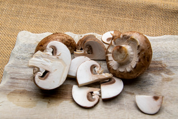 Braune Champignons, halbiert und in feine Scheiben geschnitten, liegen auf einem Holzbrett.