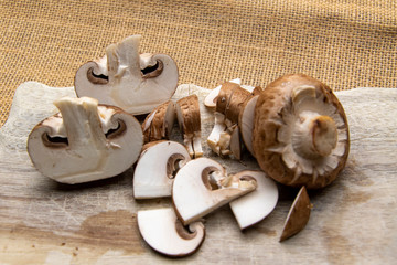 Braune Champignons, halbiert und in feine Scheiben geschnitten, liegen auf einem Holzbrett.